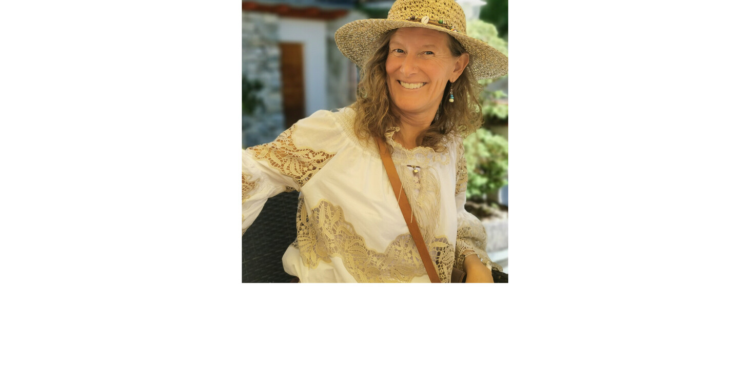 Frau mit strohfarbenem Hut und weißer Bluse mit Spitzenmuster sitzt an einem Tisch im Freien.