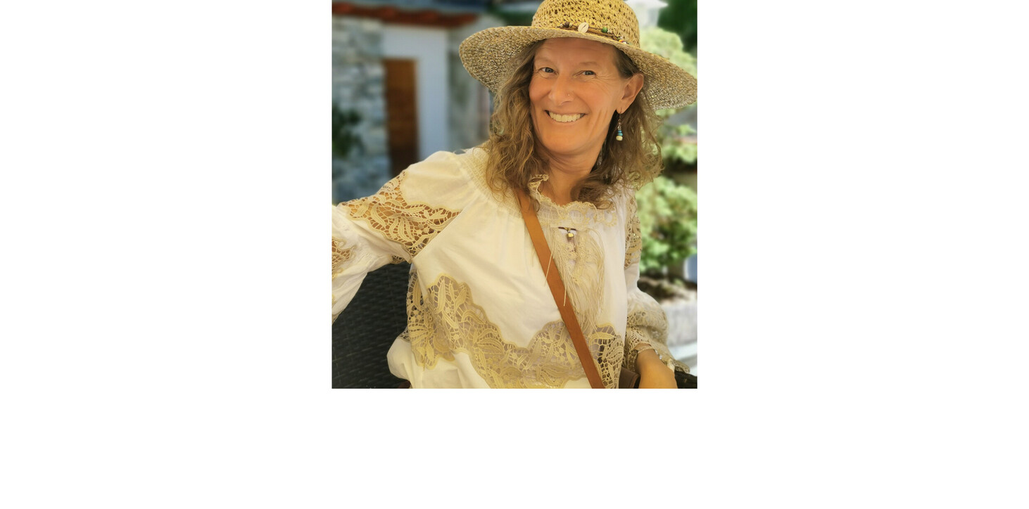 Frau mit strohfarbenem Hut und weißer Bluse mit Spitzenmuster sitzt an einem Tisch im Freien.